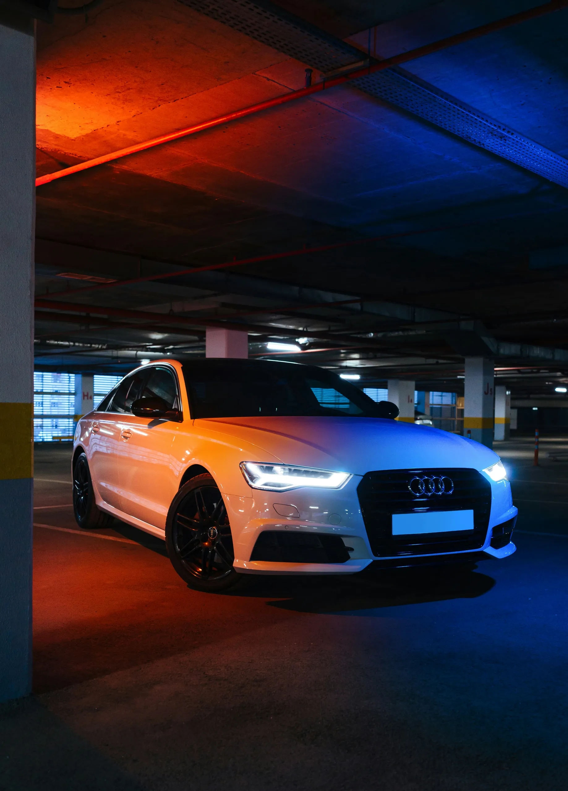 Białe Audi A6 na parkingu podziemnym w neonowym oświetleniu